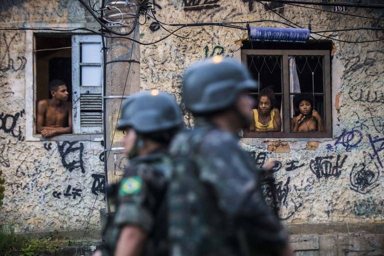 Moradores observam homens das Forças Armadas no complexo do Chapadão, na zona norte do Rio, nesta segunda (26)