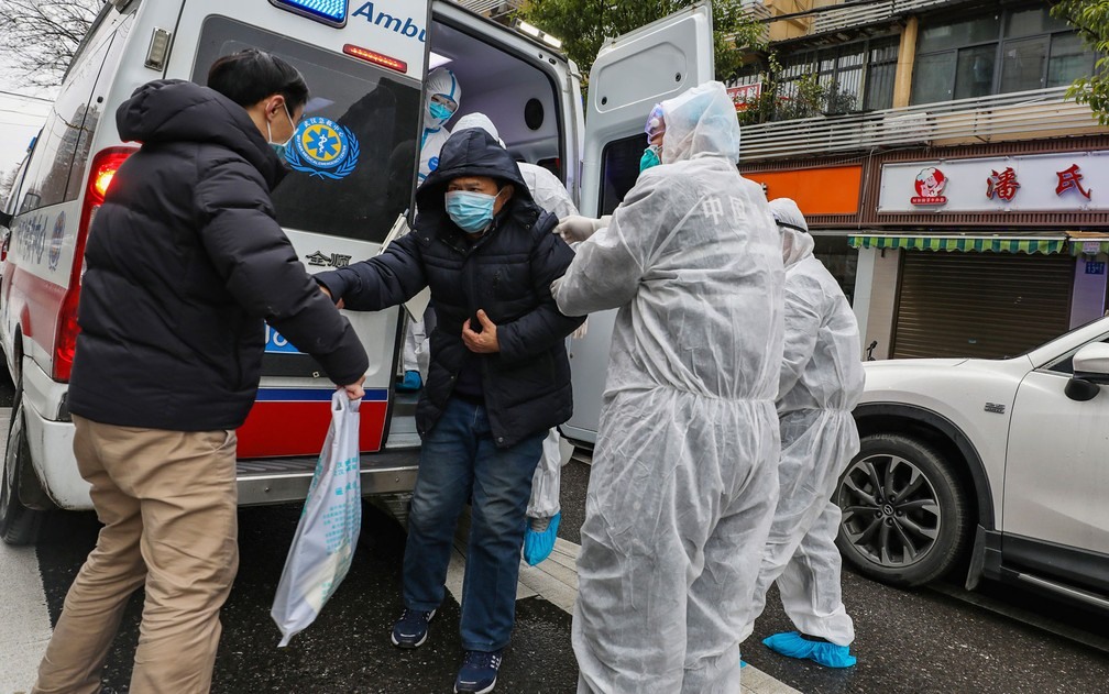 Médicos ajudam paciente a sair de uma ambulância em Euhan, na província de Hubei, na China, no domingo (26) — Foto: Chinatopix via AP