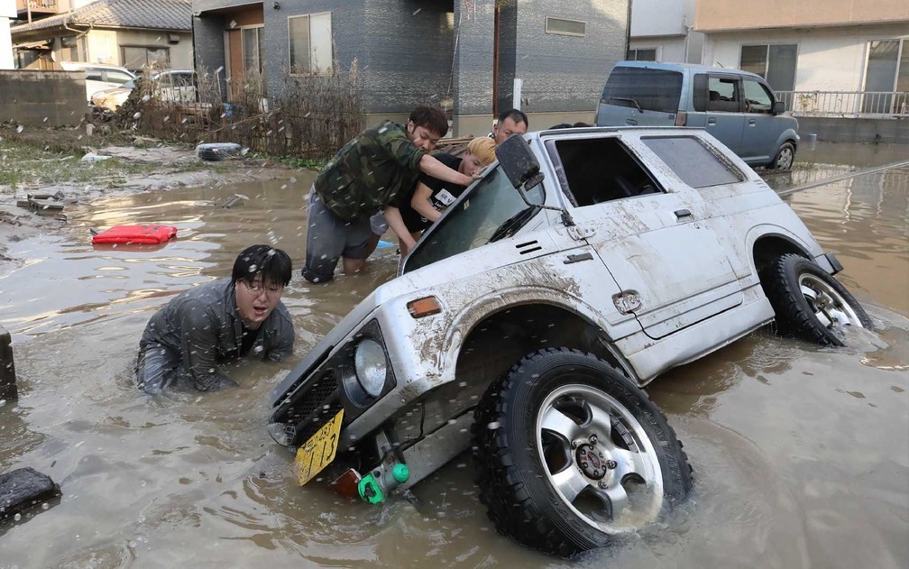 Moradores tentam erguer um veÃ­culo preso em uma Ã¡rea atingida pela enchente em Kurashiki, provÃ­ncia de Okayama (Foto: Jiji Press / via AFP Photo)