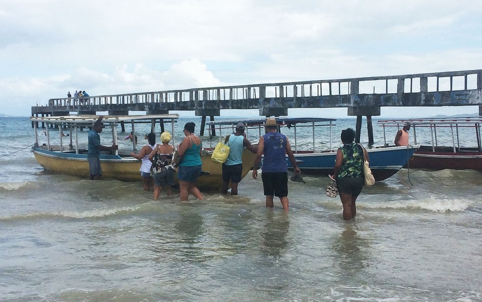 Pessoas entrando em um dos barcos pequenos pela água, na praia de São Tomé de Paripe, na capital baiana (Foto: Maiana Belo/G1 BA)