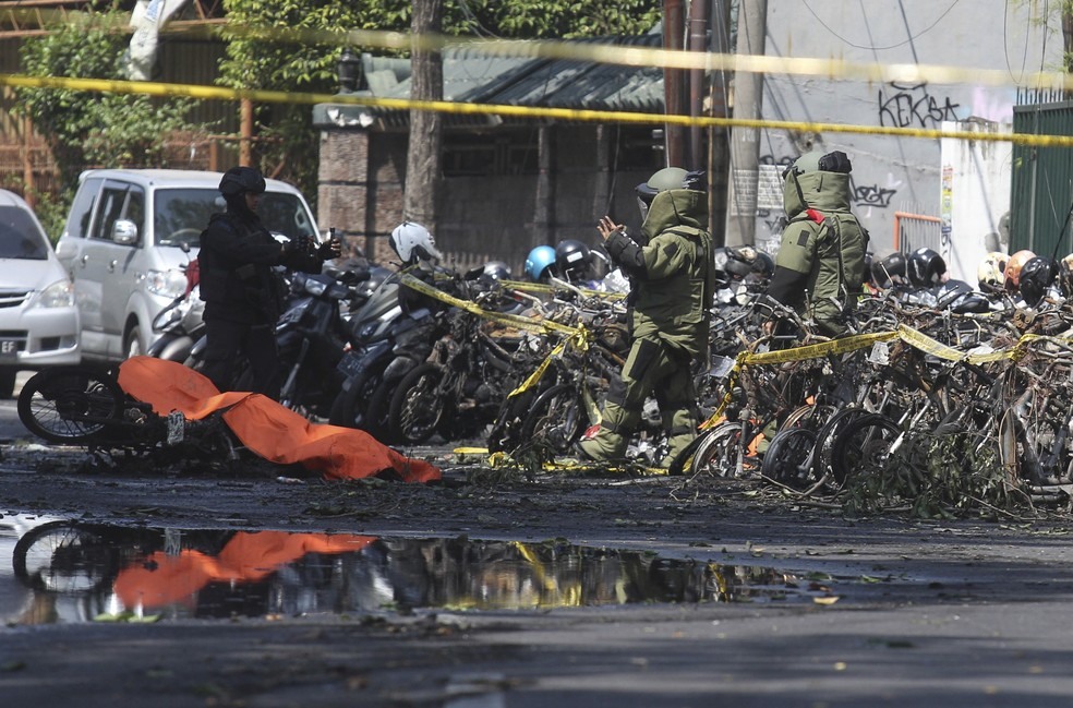 Membros do esquadrÃ£o anti-bombas da polÃ­cia inspeciona local de explosÃ£o em frente a igreja em Surabaia, na IndonÃ©sia, neste domingo (13) (Foto: Trisnadi/AP)